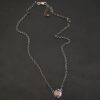 Photo of the "Ciara" Necklace. Made out of sterling silver and tourmaline. The necklace has a small tourmaline in the center, of which is a vibrant red color. The necklace has two layers of sterling silver, and both are hammered. The necklace also has three silver balls scattered around the pendant part of the necklace. There are two loops on the back of the pendant to connect the chain for the necklace to. The necklace is laying against a dark background.
