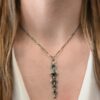 Photo of the "Nightfall" Necklace. Made out of sterling silver, gold, and diamond. There are five diamonds, all in a straight line, that create the pendant of the necklace. Each of the diamonds are different shapes, sizes, and colors. Each of these diamonds are separated by gold balls, which there are six of. The top of the pendant starts with a gold ball, then a large diamond, then a gold ball, and keeps alternating until the final diamond that has a gold ball on the end of it. There is a large loop soldered to the back of the top of the pendant with three gold jump rings attached to it. Going through the jump rings is the silver chain of the necklace. The chain of the necklace has gold loops scattered around it. Necklace is worn by a model at 16" long to demonstrate size.