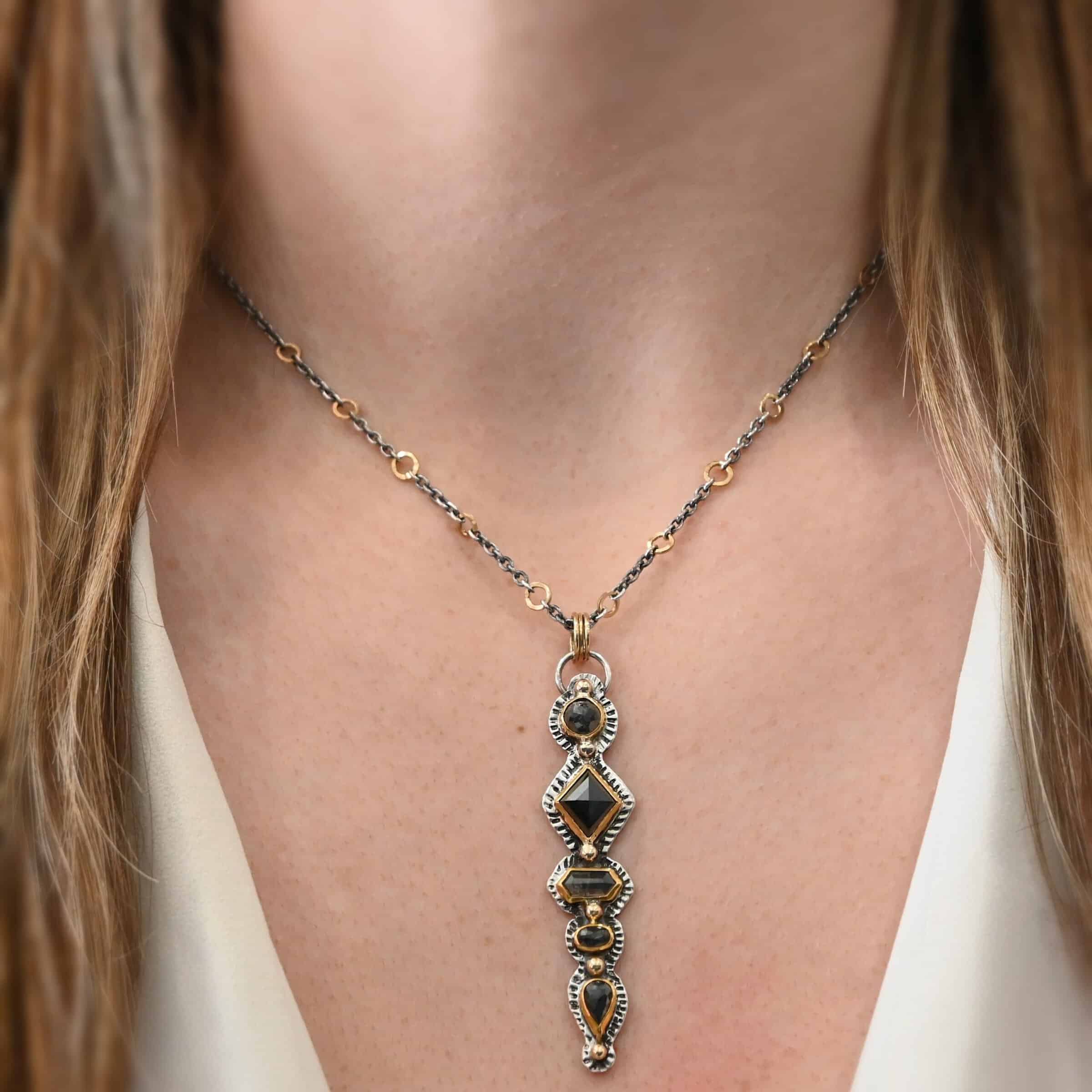 Nightfall Necklace Photo of the "Nightfall" Necklace. Made out of sterling silver, gold, and diamond. There are five diamonds, all in a straight line, that create the pendant of the necklace. Each of the diamonds are different shapes, sizes, and colors. Each of these diamonds are separated by gold balls, which there are six of. The top of the pendant starts with a gold ball, then a large diamond, then a gold ball, and keeps alternating until the final diamond that has a gold ball on the end of it. There is a large loop soldered to the back of the top of the pendant with three gold jump rings attached to it. Going through the jump rings is the silver chain of the necklace. The chain of the necklace has gold loops scattered around it. Necklace is worn by a model at 16" long to demonstrate size.