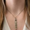 Photo of the "Daybreak" Necklace. Made out of sterling silver, gold, and diamond. There are nine diamonds, all in a straight line, that create the pendant of the necklace. Five of the diamonds are different shapes, sizes, and colors. Each of these diamonds are separated by small, circular diamonds, which there are four of. The top of the pendant starts with a large diamond, then a small one, and keeps alternating until the final diamond is a large one. There is a large loop soldered to the back of the top of the pendant with four gold jump rings attached to it. Going through the jump rings is the silver chain of the necklace. The chain of the necklace has gold loops scattered around it. Necklace is worn by a model at 16" long to demonstrate size of the pendant.