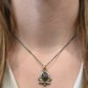 Photo of the "Golden Fields" Necklace. Made out of sterling silver, gold, sapphire, and diamonds. The center stone is an oval shaped, deep brown sapphire that is set in gold. There is a gold ball on the left and right side of this sapphire. There are also four gold leaves, two on each side, beneath the gold balls. The ends of each leaf meet, and where they meet in the center is a gold ball. There are three diamonds, two small and one big, beneath the sapphire, that the gold leaves surround. The two small diamonds are on the side with the big one in the middle. There are three more gold balls that surround each side of the big diamond. There is a loop on the back of the necklace, with three gold jump rings that are attached to it. Going through the jump rings is the chain of the necklace. Necklace is worn by a model at 17" long to demonstrate size of the necklace.
