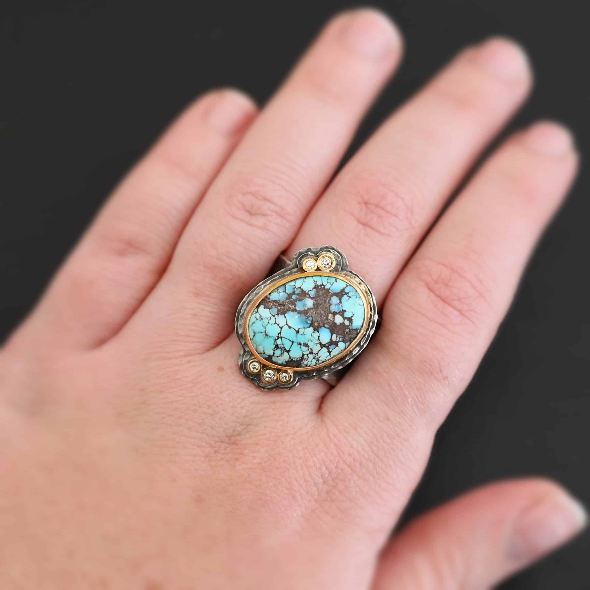 Sunshine & Blue Skies Ring "Sunshine & Blue Skies" Ring. There is a large oval shaped turquoise, set slightly askew, pointing towards the right. The turquoise is set in gold, as well as the diamonds. There are three small diamonds on the top and two on the bottom. Both follow the curve of the oval. There are two layers of sterling silver around the stone, and both are hammered. Ring band is thick silver and hammered. Ring is worn on a models middle finger.