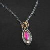 Photo of the "Soft Petals" Necklace. Made out of sterling silver, gold, ruby, and diamond. The bottom of the ring has a small circle diamond. Above this is a pink, marquise shaped ruby placed vertically, so that the points are pointing up and down. The stone is set in gold, and there are two layers of sterling silver beneath it. The top layer of silver goes around the edge of the bottom layer. Both layers are marquise shaped, and the top outside layer is hammered. There is a loop on the back of the necklace in which three gold jump rings go through. Going through the jump rings is the silver chain of the necklace. Necklace is laying against a dark background.