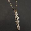 Photo of the "Nightfall" Necklace. Made out of sterling silver, gold, and diamond. There are five diamonds, all in a straight line, that create the pendant of the necklace. Each of the diamonds are different shapes, sizes, and colors. Each of these diamonds are separated by gold balls, which there are six of. The top of the pendant starts with a gold ball, then a large diamond, then a gold ball, and keeps alternating until the final diamond that has a gold ball on the end of it. There is a large loop soldered to the back of the top of the pendant with three gold jump rings attached to it. Going through the jump rings is the silver chain of the necklace. The chain of the necklace has gold loops scattered around it. Necklace is lying against a dark background.