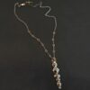 Photo of the "Nightfall" Necklace. Made out of sterling silver, gold, and diamond. There are five diamonds, all in a straight line, that create the pendant of the necklace. Each of the diamonds are different shapes, sizes, and colors. Each of these diamonds are separated by gold balls, which there are six of. The top of the pendant starts with a gold ball, then a large diamond, then a gold ball, and keeps alternating until the final diamond that has a gold ball on the end of it. There is a large loop soldered to the back of the top of the pendant with three gold jump rings attached to it. Going through the jump rings is the silver chain of the necklace. The chain of the necklace has gold loops scattered around it. Necklace is lying against a dark background.