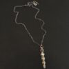 Photo of the "Daybreak" Necklace. Made out of sterling silver, gold, and diamond. There are nine diamonds, all in a straight line, that create the pendant of the necklace. Five of the diamonds are different shapes, sizes, and colors. Each of these diamonds are separated by small, circular diamonds, which there are four of. The top of the pendant starts with a large diamond, then a small one, and keeps alternating until the final diamond is a large one. There is a large loop soldered to the back of the top of the pendant with four gold jump rings attached to it. Going through the jump rings is the silver chain of the necklace. The chain of the necklace has gold loops scattered around it. Necklace is lying against a dark background.