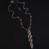 Photo of the "Nightfall" Necklace. Made out of sterling silver, gold, and diamond. There are five diamonds, all in a straight line, that create the pendant of the necklace. Each of the diamonds are different shapes, sizes, and colors. Each of these diamonds are separated by gold balls, which there are six of. The top of the pendant starts with a gold ball, then a large diamond, then a gold ball, and keeps alternating until the final diamond that has a gold ball on the end of it. There is a large loop soldered to the back of the top of the pendant with three gold jump rings attached to it. Going through the jump rings is the silver chain of the necklace. The chain of the necklace has gold loops scattered around it. Necklace is lying against a dark background.