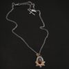 Photo of the "Golden Fields" Necklace. Made out of sterling silver, gold, sapphire, and diamonds. The center stone is an oval shaped, deep brown sapphire that is set in gold. There is a gold ball on the left and right side of this sapphire. There are also four gold leaves, two on each side, beneath the gold balls. The ends of each leaf meet, and where they meet in the center is a gold ball. There are three diamonds, two small and one big, beneath the sapphire, that the gold leaves surround. The two small diamonds are on the side with the big one in the middle. There are three more gold balls that surround each side of the big diamond. There is a loop on the back of the necklace, with three gold jump rings that are attached to it. Going through the jump rings is the chain of the necklace. Necklace is lying against a dark background.