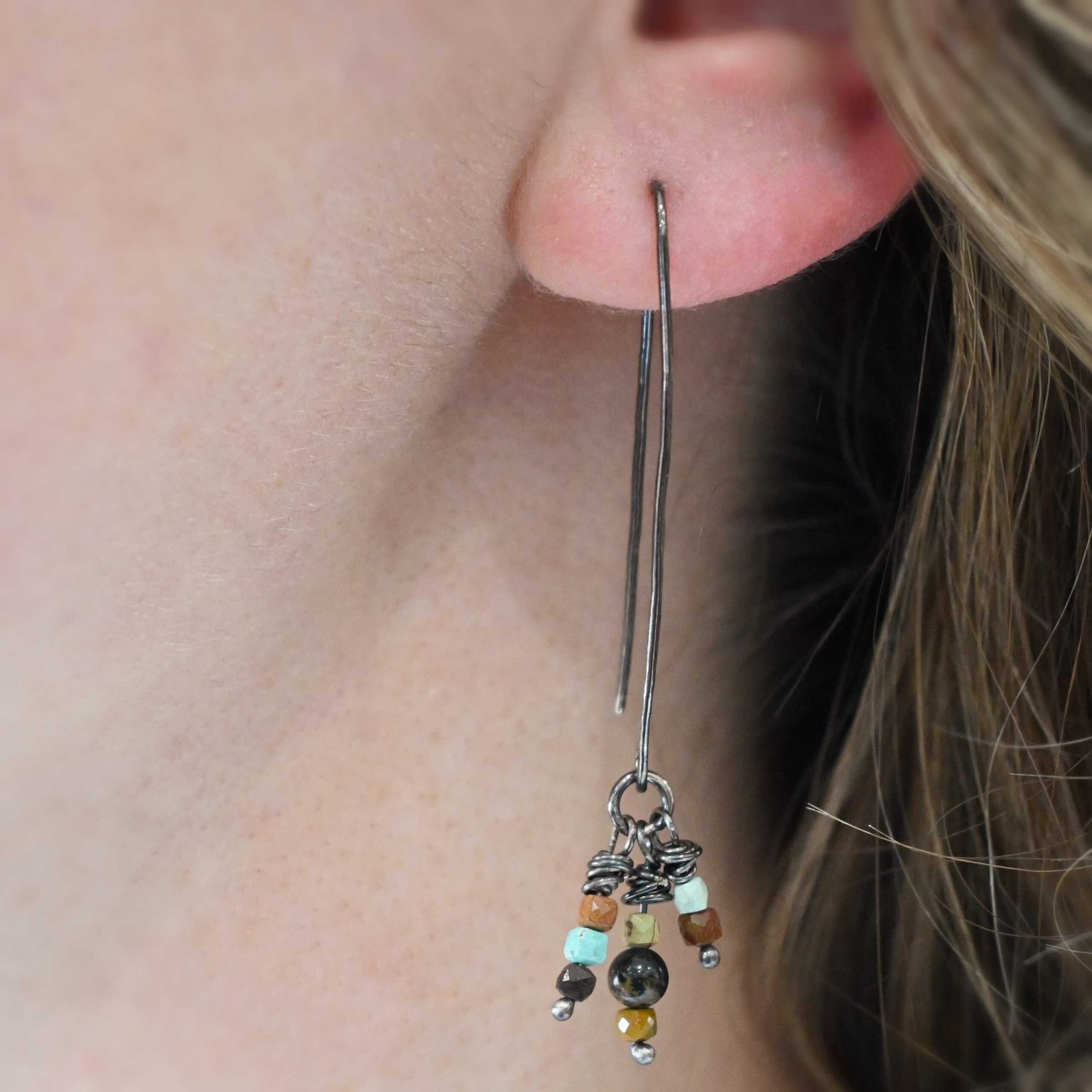 "Imber" Earring shown on a model. Each earring is an upside down "U" Shape. Earring has three small strands of silver hanging down from it, each with three beads on it. Each strand has silver wrapped around the top.