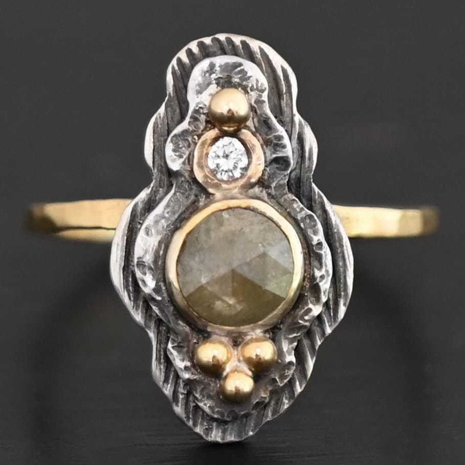 Garden Of Eden Ring New Photo of the "Garden Of Eden" Ring. Made out of sterling silver and diamonds. There is a ball of gold on the top and a small, clear, circular diamond beneath it. Then, a larger, darker green, circular diamond, and three balls of gold beneath that in a triangle shape. There are two layers of silver, both with hammered lines in them. The band is thin gold that is hammered.