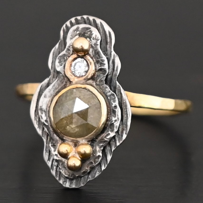 Garden Of Eden Ring New Photo of the "Garden Of Eden" Ring. Made out of sterling silver and diamonds. There is a ball of gold on the top and a small, clear, circular diamond beneath it. Then, a larger, darker green, circular diamond, and three balls of gold beneath that in a triangle shape. There are two layers of silver, both with hammered lines in them. The band is thin gold that is hammered.