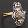 Photo of the "Garden Of Eden" Ring. Made out of sterling silver and diamonds. There is a ball of gold on the top and a small, clear, circular diamond beneath it. Then, a larger, darker green, circular diamond, and three balls of gold beneath that in a triangle shape. There are two layers of silver, both with hammered lines in them. The band is thin gold that is hammered.