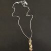 Photo of the "Music Of The Night" Necklace. Made out of sterling silver, gold, and diamonds. The top of the pendant, on the back, has a silver loop soldered to it with two gold jump rings that each end of the chain is attached to. There is gold ball detail that swirls back and forth all the way down the pendant. There is a line of hammered gold that also swirls around the pendant, but opposite of the gold balls, so they intertwine and intercept each other. There are eight diamonds on the pendant. Four of them are larger, and go in a straight line down the pendant. The other four are scattered around them. The gold line and gold balls twirl around each of the diamonds on opposite sides. Necklace is lying against a dark background.