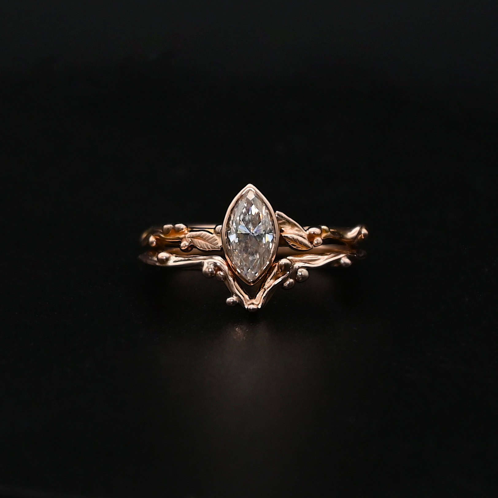 "Forrest Bride" Ring. There is a marquise shaped diamond in the center of the top band. The band is rose gold and has rose gold leaves and balls all around the band. The bottom band has a dip in the center to fit around the bottom of the marquise. This band has balls of rose gold around it as well.