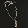 Photo of the "Music Of The Night" Necklace. Made out of sterling silver, gold, and diamonds. The top of the pendant, on the back, has a silver loop soldered to it with two gold jump rings that each end of the chain is attached to. There is gold ball detail that swirls back and forth all the way down the pendant. There is a line of hammered gold that also swirls around the pendant, but opposite of the gold balls, so they intertwine and intercept each other. There are eight diamonds on the pendant. Four of them are larger, and go in a straight line down the pendant. The other four are scattered around them. The gold line and gold balls twirl around each of the diamonds on opposite sides. Necklace is lying against a dark background.