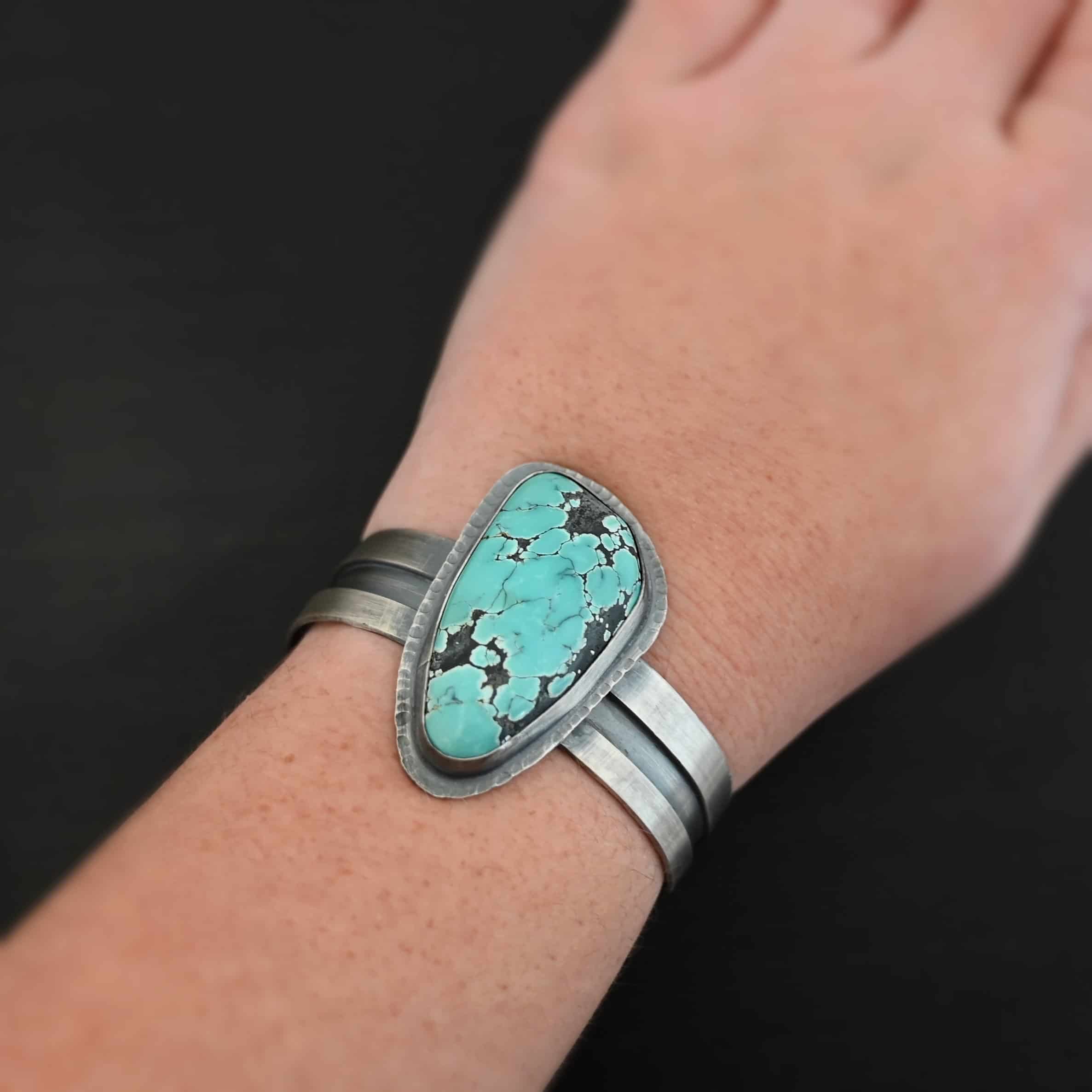 Mountains Are Calling Cuff "Mountains Are Calling" Cuff. There is a large, oval shaped turquoise in the center with hammered sterling silver around the stone. The band of the cuff is thick and oxidized. The entire center of the cuff has a thick rectangular line that is cut out and oxidized deeper than the rest of the cuff. Cuff is worn by a model.