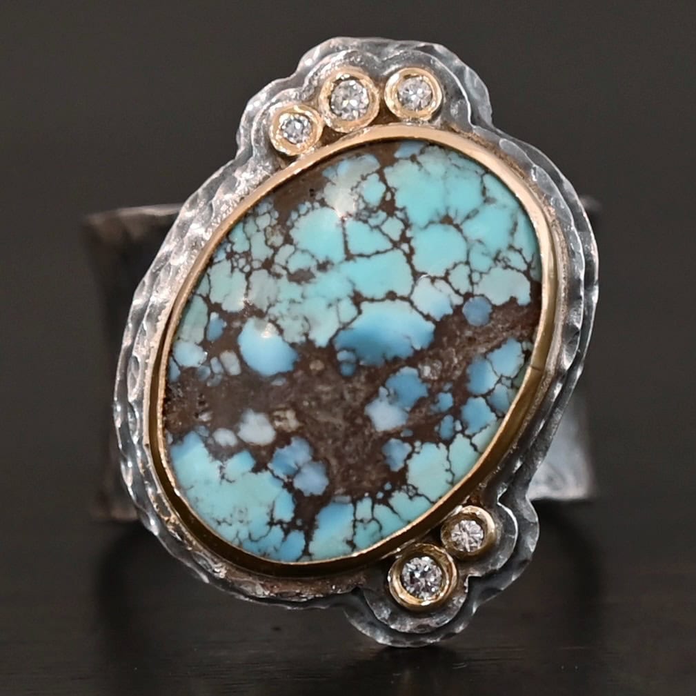 Sunshine and Blue Skies Ring "Sunshine & Blue Skies" Ring. There is a large oval shaped turquoise, set slightly askew, pointing towards the right. The turquoise is set in gold, as well as the diamonds. There are three small diamonds on the top and two on the bottom. Both follow the curve of the oval. There are two layers of sterling silver around the stone, and both are hammered. Ring band is thick silver and hammered.