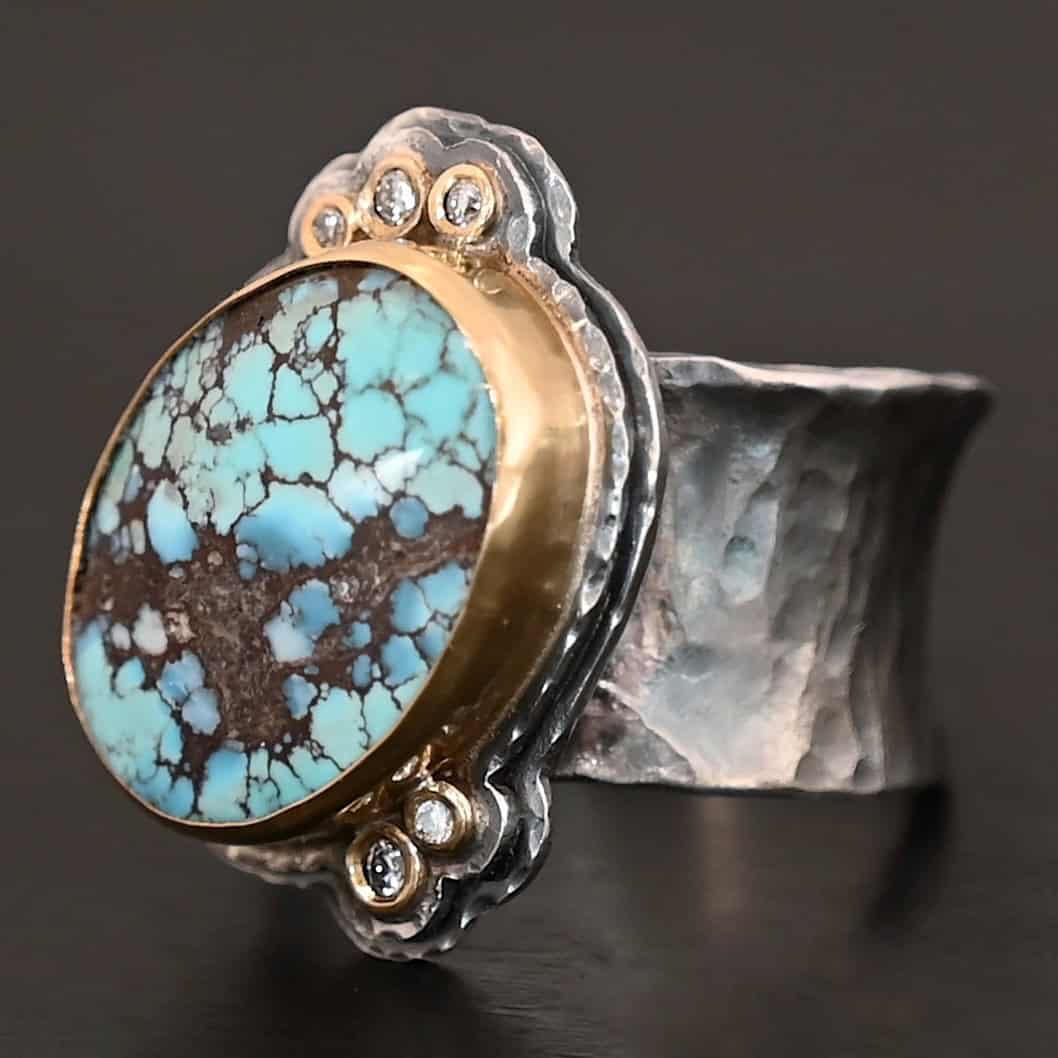 Sunshine and Blue Skies Ring "Sunshine & Blue Skies" Ring. There is a large oval shaped turquoise, set slightly askew, pointing towards the right. The turquoise is set in gold, as well as the diamonds. There are three small diamonds on the top and two on the bottom. Both follow the curve of the oval. There are two layers of sterling silver around the stone, and both are hammered. Ring band is thick silver and hammered.