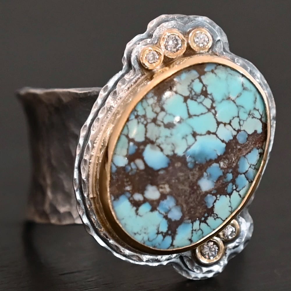 Sunshine and Blue Skies Ring "Sunshine & Blue Skies" Ring. There is a large oval shaped turquoise, set slightly askew, pointing towards the right. The turquoise is set in gold, as well as the diamonds. There are three small diamonds on the top and two on the bottom. Both follow the curve of the oval. There are two layers of sterling silver around the stone, and both are hammered. Ring band is thick silver and hammered.