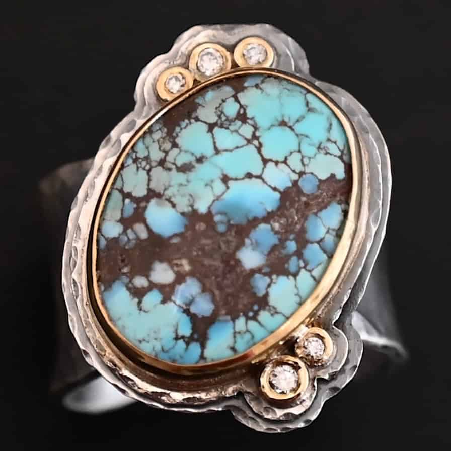 Sunshine and Blue Skies Ring "Sunshine & Blue Skies" Ring. There is a large oval shaped turquoise, set slightly askew, pointing towards the right. The turquoise is set in gold, as well as the diamonds. There are three small diamonds on the top and two on the bottom. Both follow the curve of the oval. There are two layers of sterling silver around the stone, and both are hammered. Ring band is thick silver and hammered.