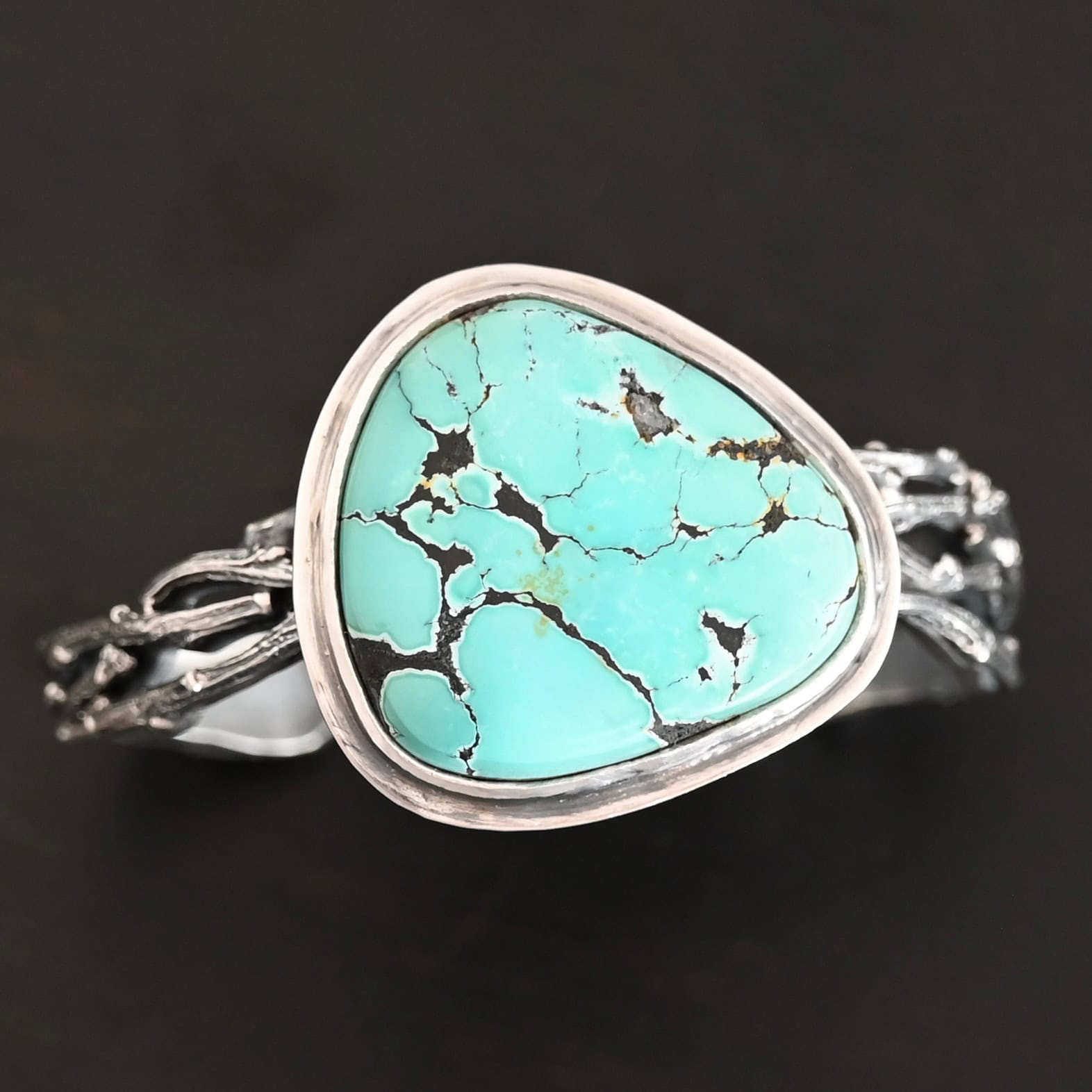 Under The Big Sky Cuff "Under The Big Sky" Cuff. There is a very large, mostly circular turquoise in the center of a thick cuff. The cuff is multiple casted sterling silver twigs that are soldered together and create a cuff.