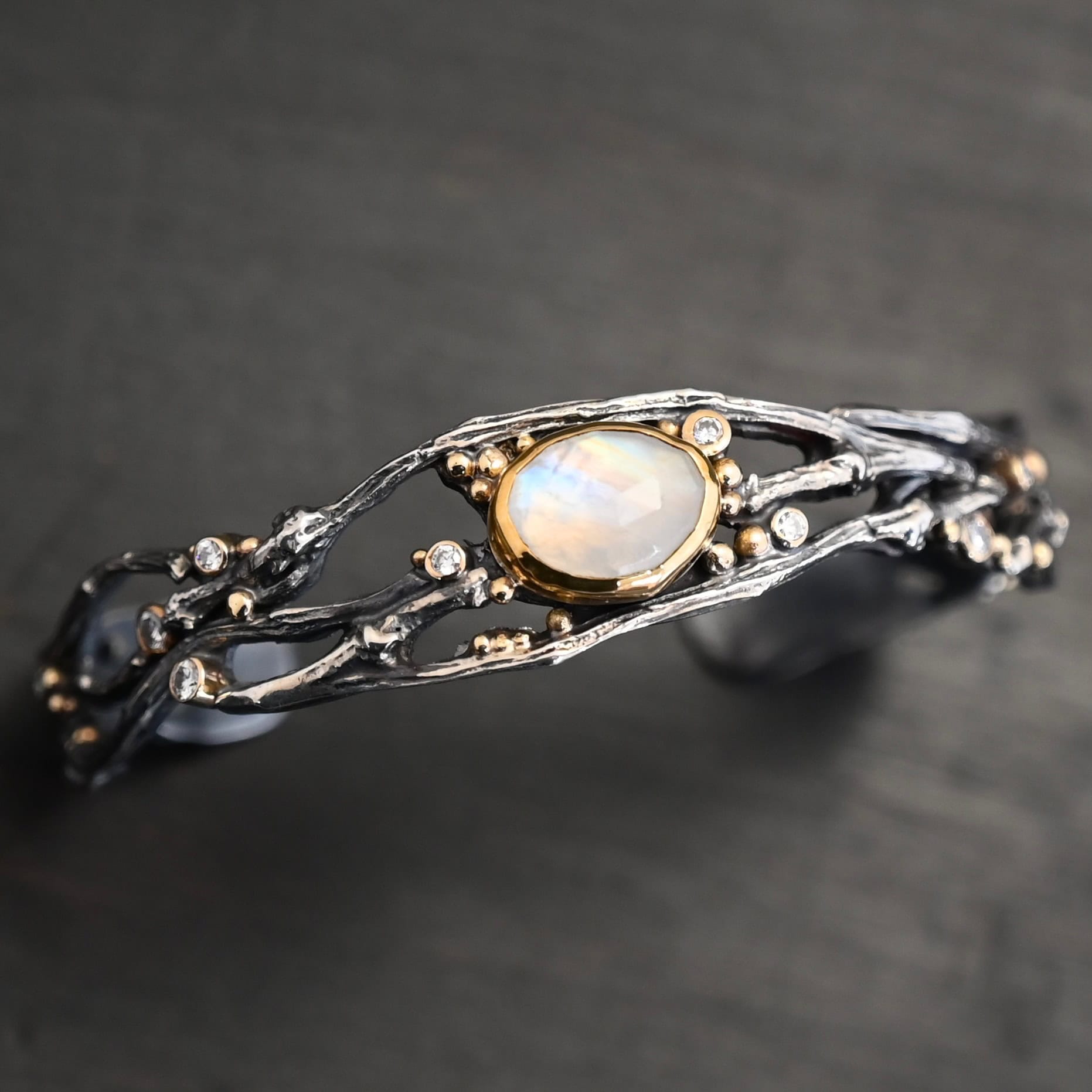 Night Flowers Cuff "Night Flowers" Cuff. There is a moonstone set in gold in the center of a cuff. The band of the cuff is multiple casted sterling silver twigs that intercept. There are small diamonds scattered around it, as well as gold ball detail.