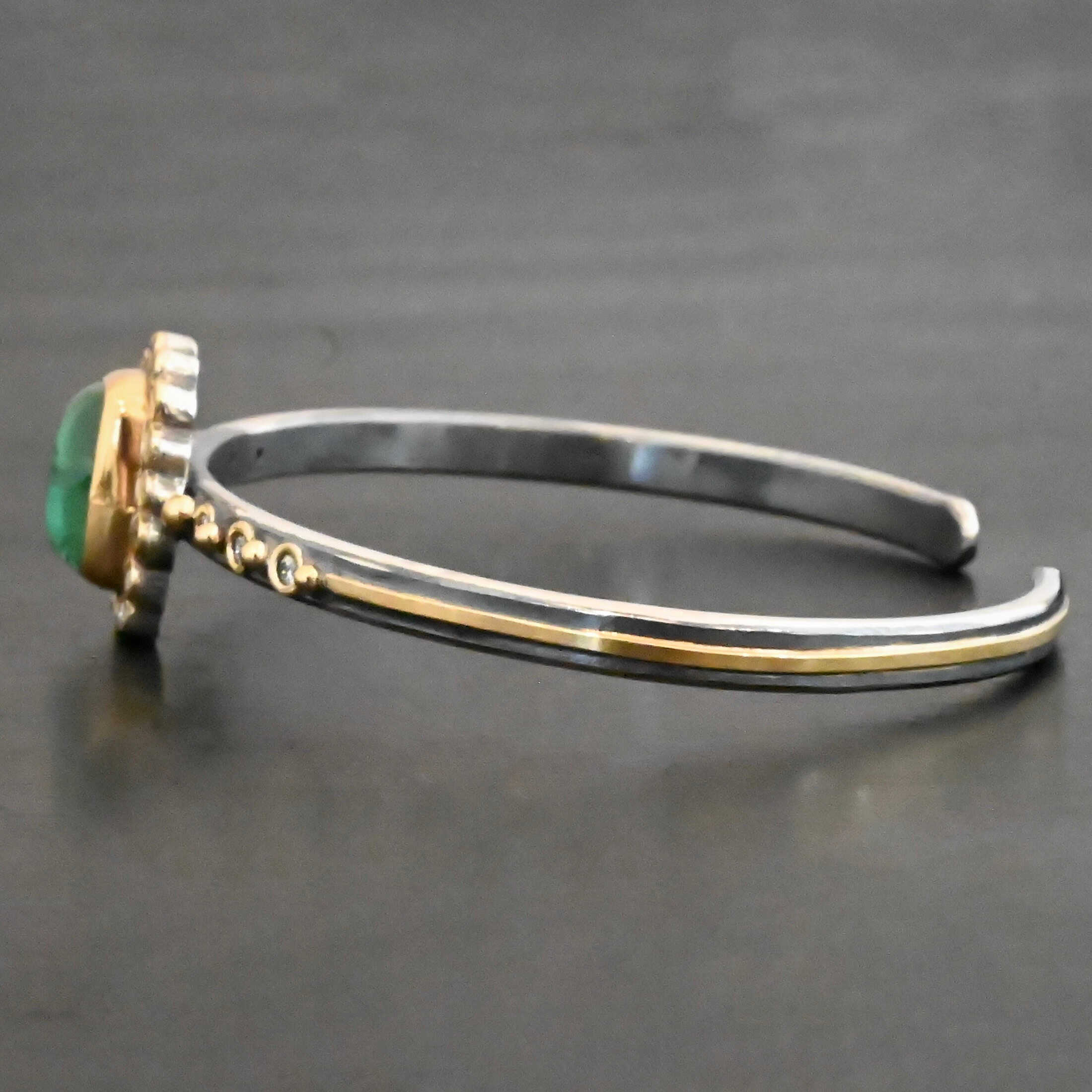 "Secret Of The Sea" Cuff. There is a rectangular, vertical tourmaline in the center, set in gold, with small diamonds surrounding the entire tourmaline. There are seventeen diamonds around the tourmaline. There are six more, three on each side of the cuff. There is gold ball detail between each diamond, and a stripe of gold that goes across the rest of the cuff.