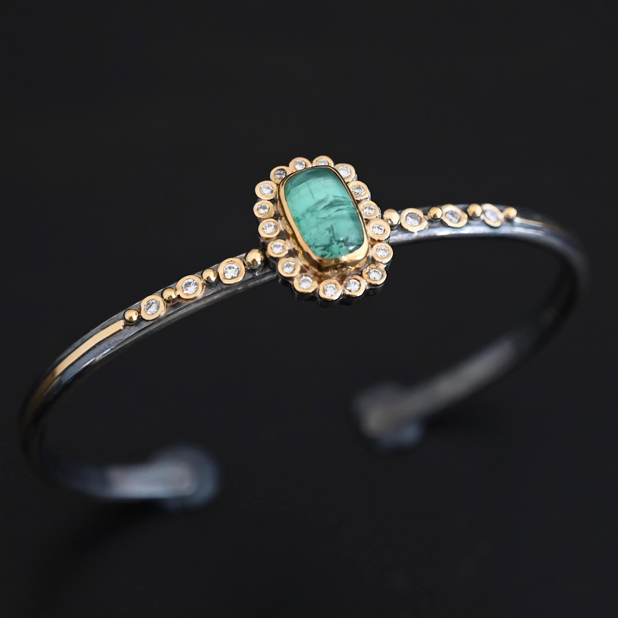 "Secret Of The Sea" Cuff. There is a rectangular, vertical tourmaline in the center, set in gold, with small diamonds surrounding the entire tourmaline. There are seventeen diamonds around the tourmaline. There are six more, three on each side of the cuff. There is gold ball detail between each diamond, and a stripe of gold that goes across the rest of the cuff.