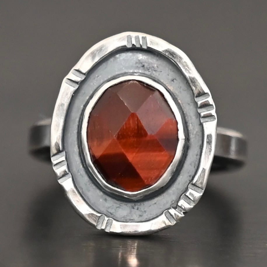 Ember Ring Photo of the "Ember" Ring. There is an oval, rose cut pietersite in the center. There is a ring of silver around it that is smooth and oxidized. There is another ring of silver around this that is lightly hammered with lines around it, and lightly oxidized.