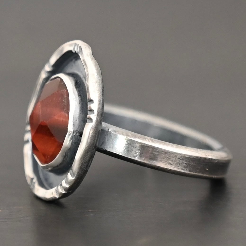 Ember Ring Photo of the "Ember" Ring. There is an oval, rose cut pietersite in the center. There is a ring of silver around it that is smooth and oxidized. There is another ring of silver around this that is lightly hammered with lines around it, and lightly oxidized.