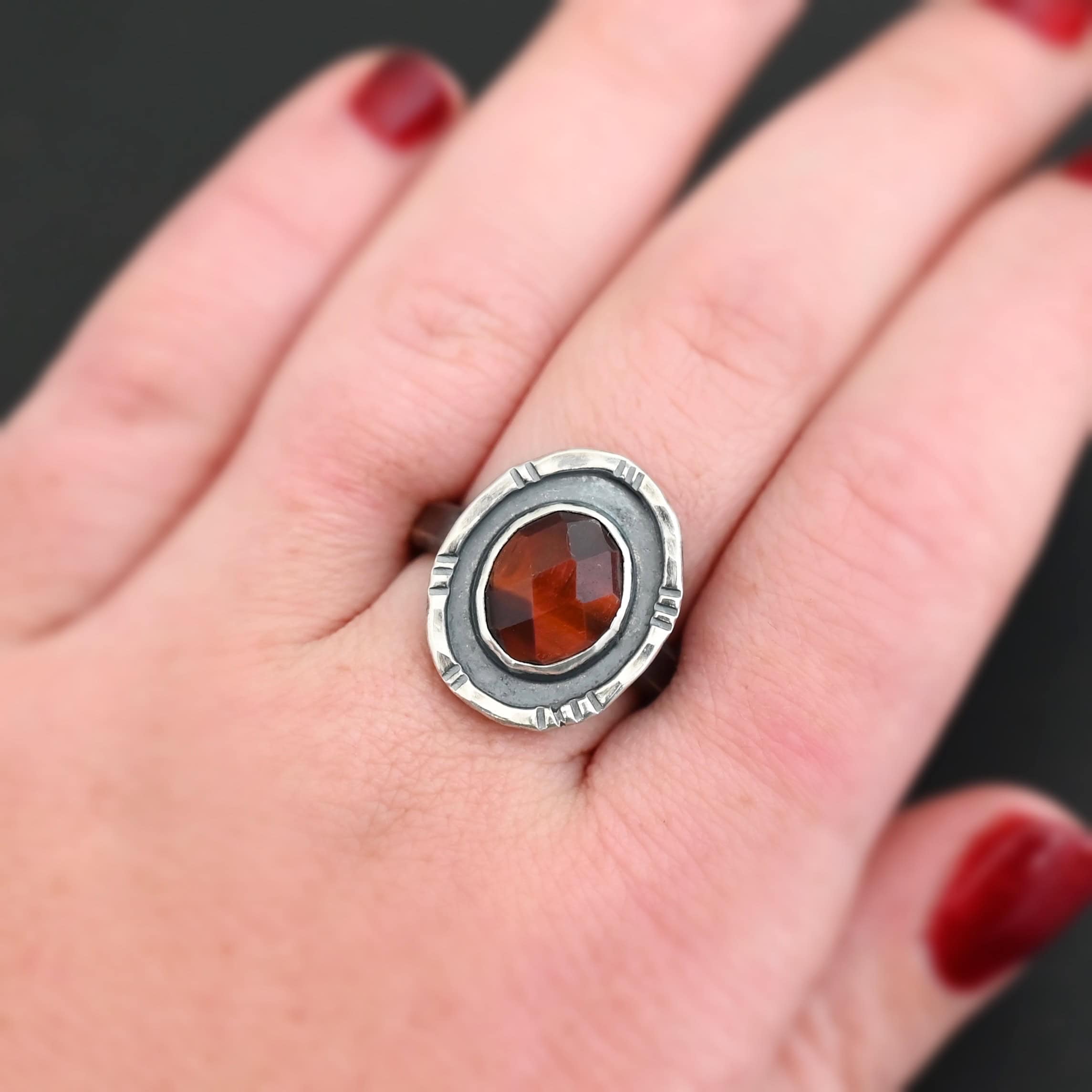 Ember Ring Photo of the "Ember" Ring. There is an oval, rose cut pietersite in the center. There is a ring of silver around it that is smooth and oxidized. There is another ring of silver around this that is lightly hammered with lines around it, and lightly oxidized.