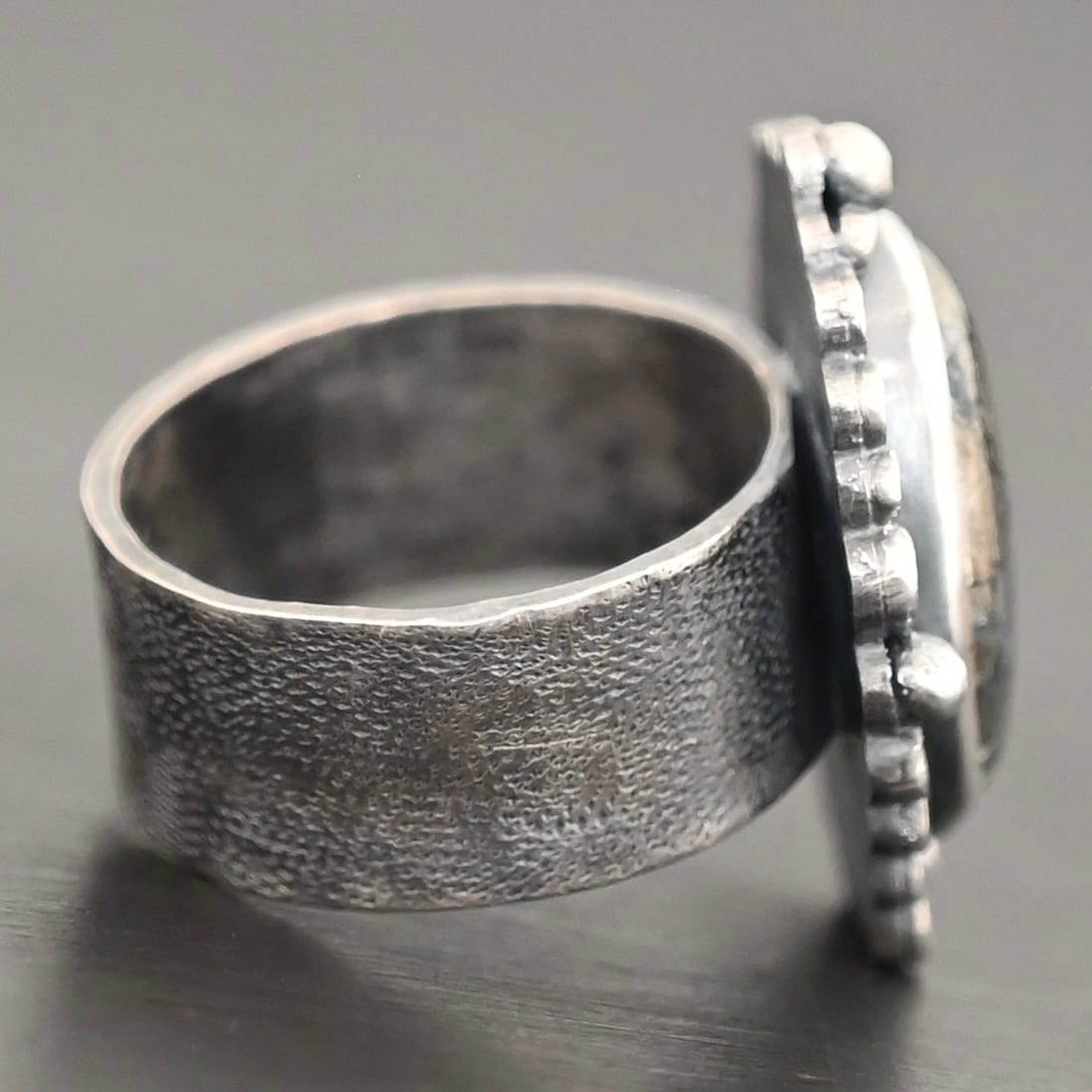 Vesper Ring Photo of the "Vesper" Ring. There is a large, oval shaped marcasite stone in the center, with both balls of silver and raised dots of silver traveling all the way around the oval stone. Ring band is thick, and hammered with small dots all the way around.