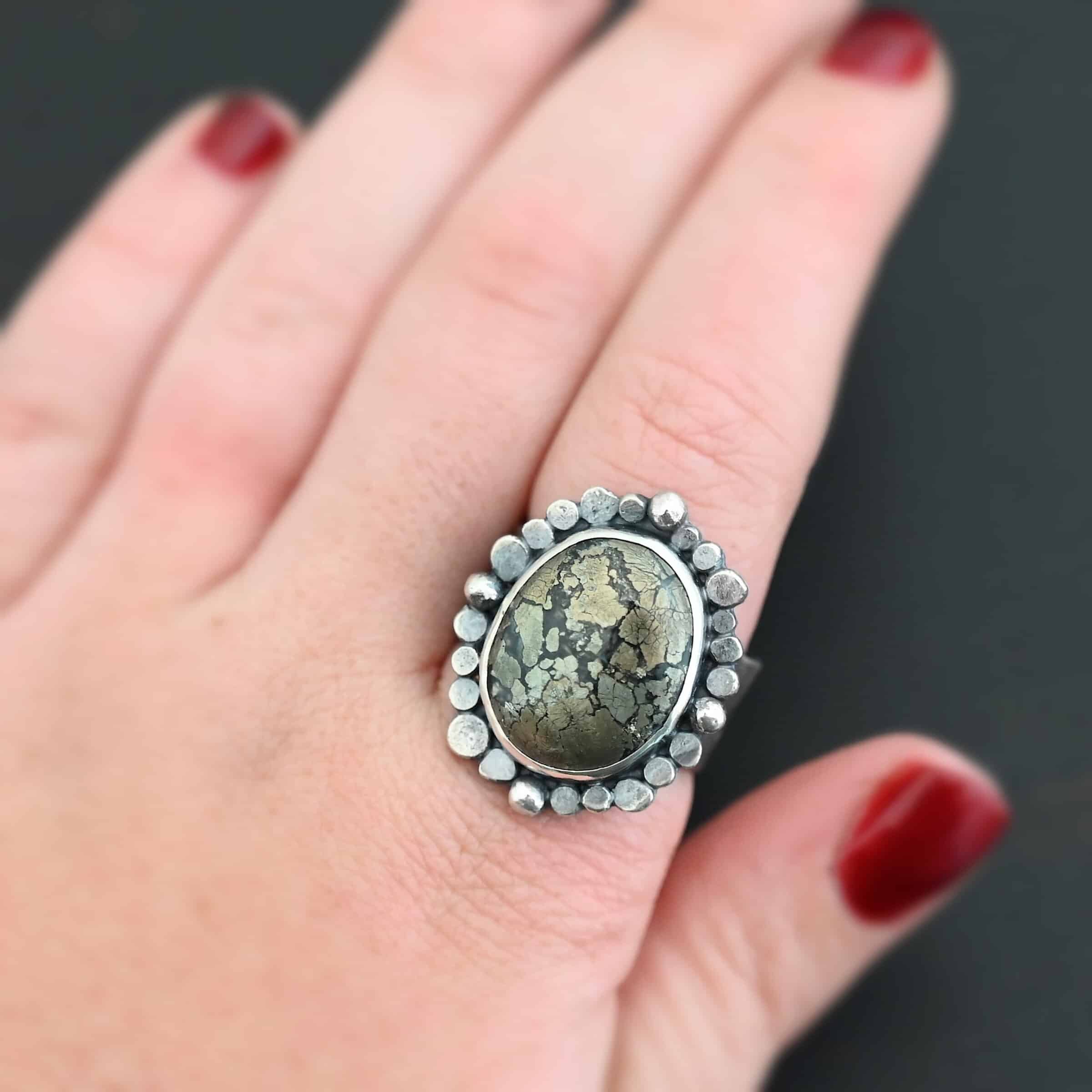 Vesper Ring Photo of the "Vesper" Ring. There is a large, oval shaped marcasite stone in the center, with both balls of silver and raised dots of silver traveling all the way around the oval stone. Ring is worn by a model up close to demonstrate size.