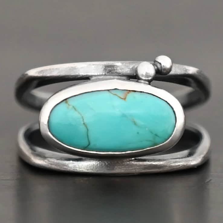 Give You The Sky Ring Photo of the "Give You The Sky" Ring. Made out of sterling silver and turquoise. The ring band is two thin, square shaped bands that meet at the back to make a hollow centered band. In the center of the ring, to fill the hollowness, is a horizontally shaped turquoise oval stone. There are two balls of silver above it on the top band.