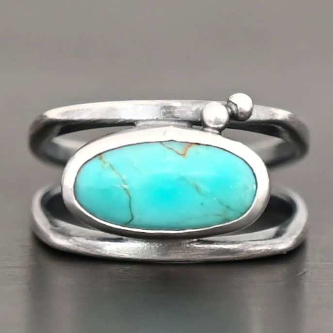 Give You The Sky Ring Photo of the "Give You The Sky" Ring. Made out of sterling silver and turquoise. The ring band is two thin, square shaped bands that meet at the back to make a hollow centered band. In the center of the ring, to fill the hollowness, is a horizontally shaped turquoise oval stone. There are two balls of silver above it on the top band.