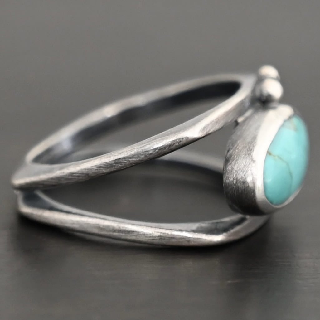 Give You The Sky Ring Photo of the "Give You The Sky" Ring. Made out of sterling silver and turquoise. The ring band is two thin, square shaped bands that meet at the back to make a hollow centered band. In the center of the ring, to fill the hollowness, is a horizontally shaped turquoise oval stone. There are two balls of silver above it on the top band.