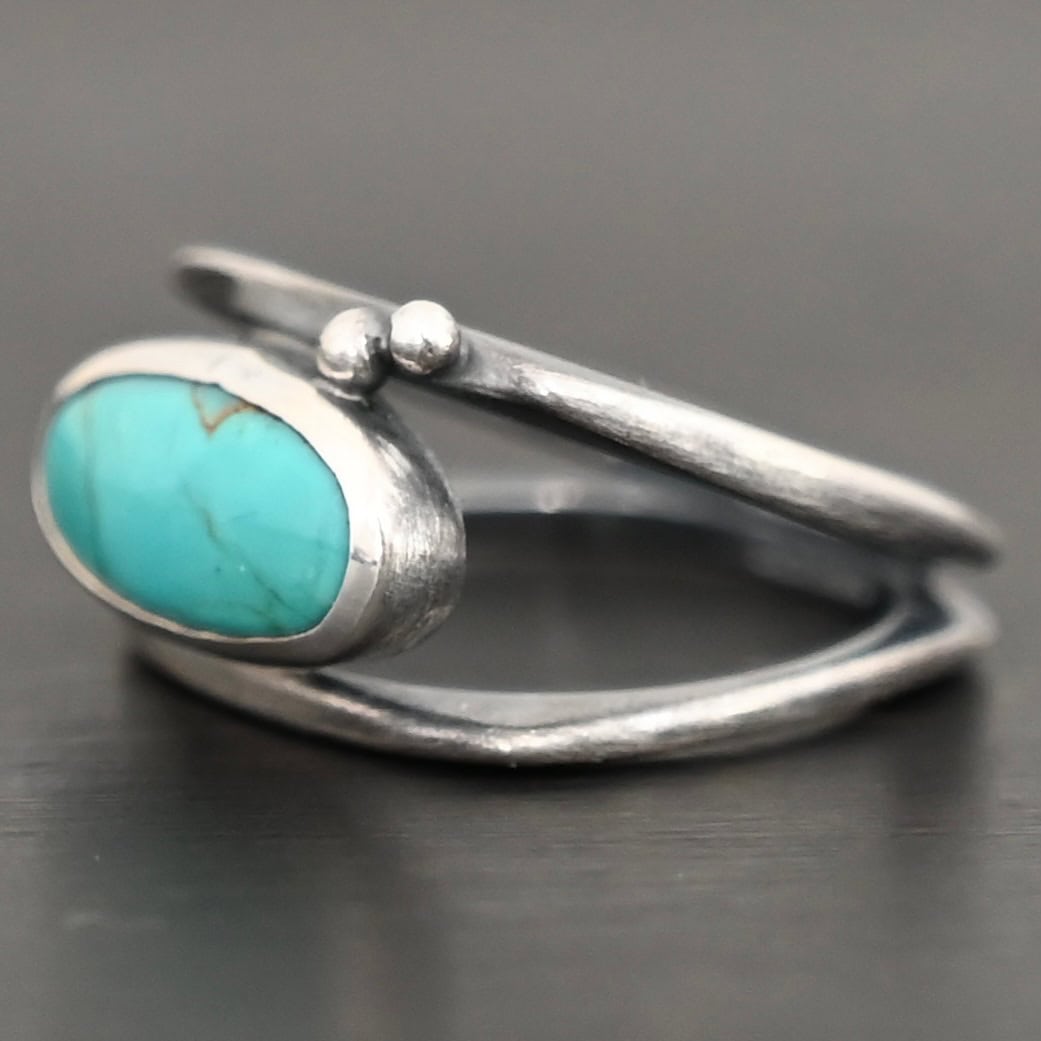 Give You The Sky Ring Photo of the "Give You The Sky" Ring. Made out of sterling silver and turquoise. The ring band is two thin, square shaped bands that meet at the back to make a hollow centered band. In the center of the ring, to fill the hollowness, is a horizontally shaped turquoise oval stone. There are two balls of silver above it on the top band.