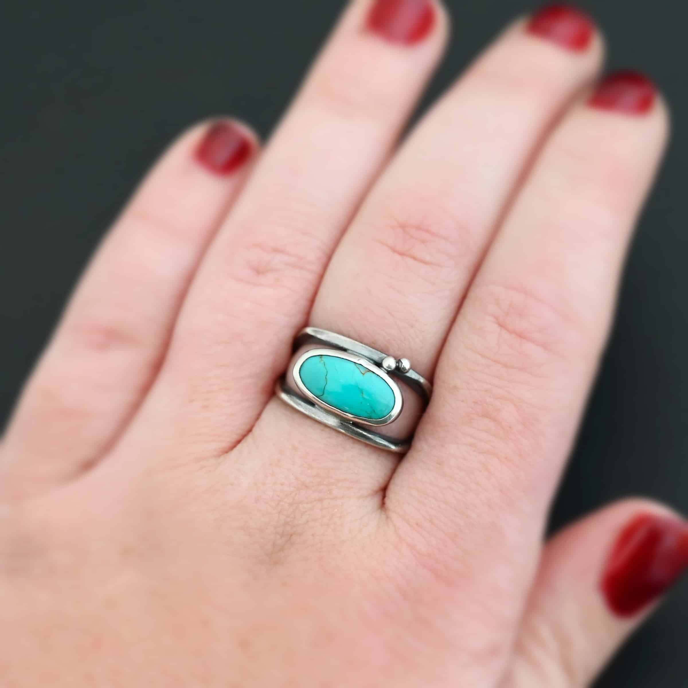 Give You The Sky Ring Photo of the "Give You The Sky" Ring. Made out of sterling silver and turquoise. The ring band is two thin, square shaped bands that meet at the back to make a hollow centered band. In the center of the ring, to fill the hollowness, is a horizontally shaped turquoise oval stone. There are two balls of silver above it on the top band.