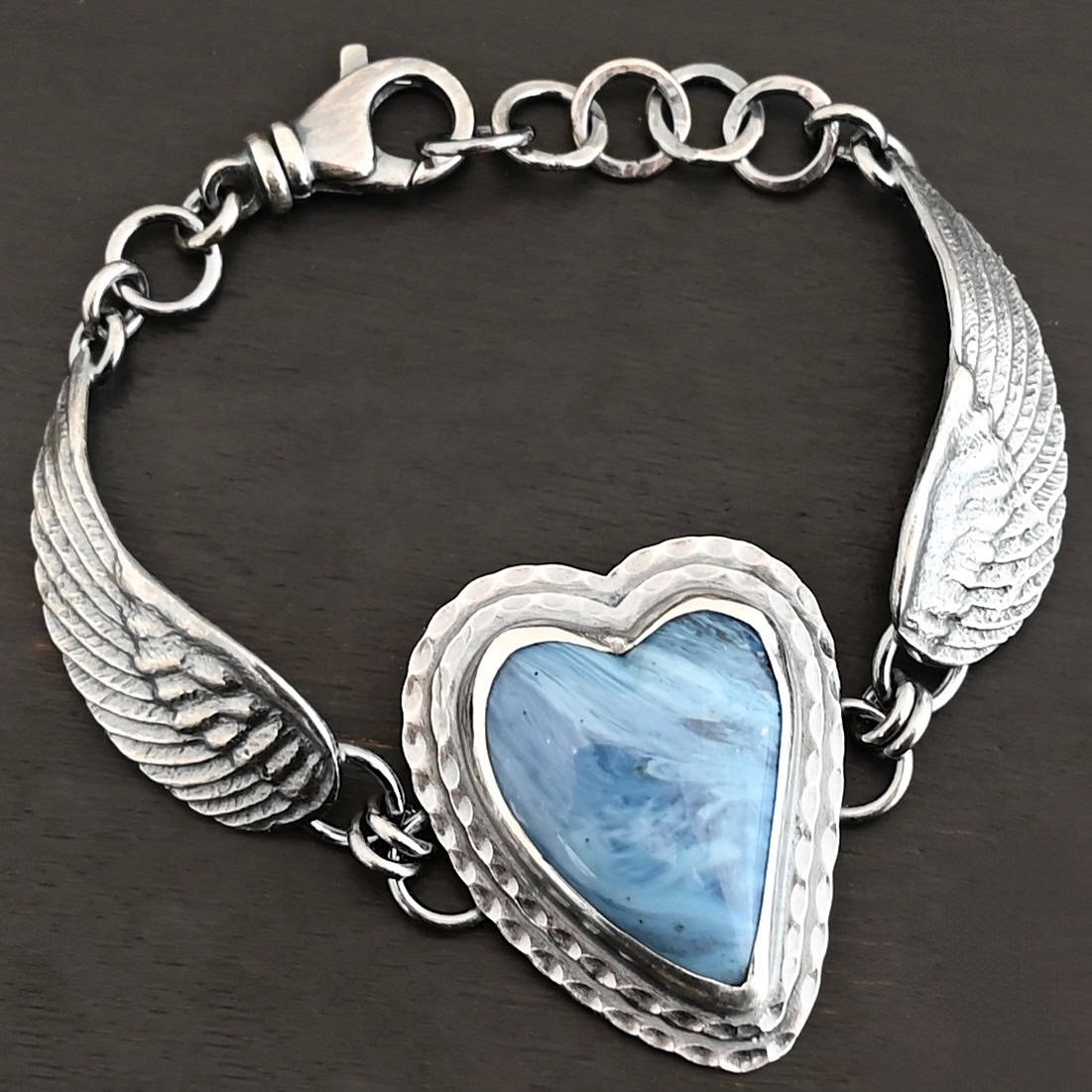 Waves Of Love Bracelet "Waves Of Love" Bracelet. The bracelet is a Leland Blue heart with medium sized angel wings on each side. The angel wings curve lightly so they can fit around the wrist. There is two layers of hammered sterling silver around the heart. Bracelet has a silver lobster claw clasp.