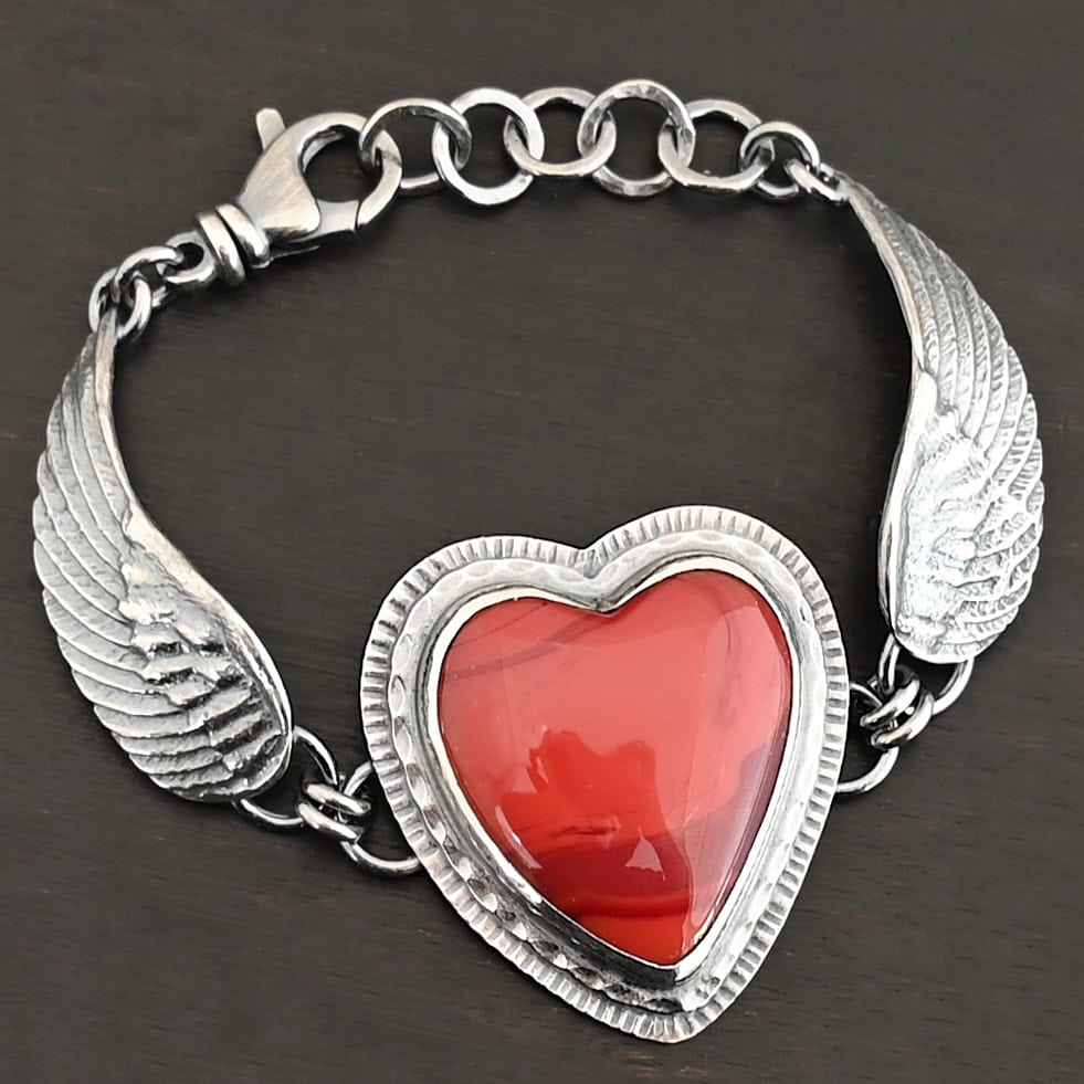 "Cerise" Bracelet. The bracelet is a rosarita heart with medium sized angel wings on each side. The angel wings curve lightly so they can fit around the wrist. There is two layers of hammered sterling silver around the heart. Bracelet has a silver lobster claw clasp.