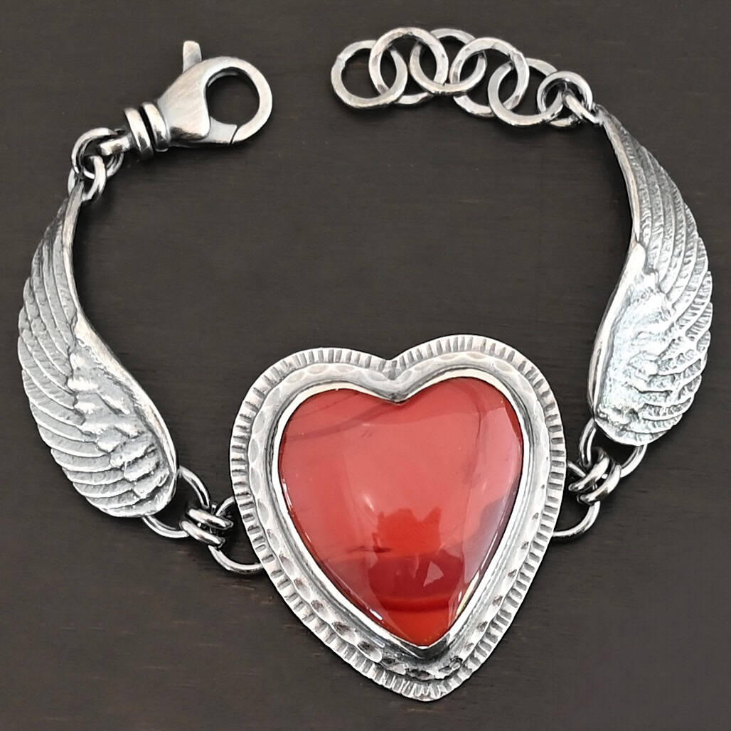 "Cerise" Bracelet. The bracelet is a rosarita heart with medium sized angel wings on each side. The angel wings curve lightly so they can fit around the wrist. There is two layers of hammered sterling silver around the heart. Bracelet has a silver lobster claw clasp.