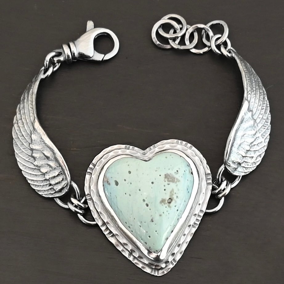 Vanessa Bracelet "Vanessa" Bracelet. The bracelet is a Leland Blue heart with medium sized angel wings on each side. The angel wings curve lightly so they can fit around the wrist. There is two layers of hammered sterling silver around the heart. Bracelet has a silver lobster claw clasp.