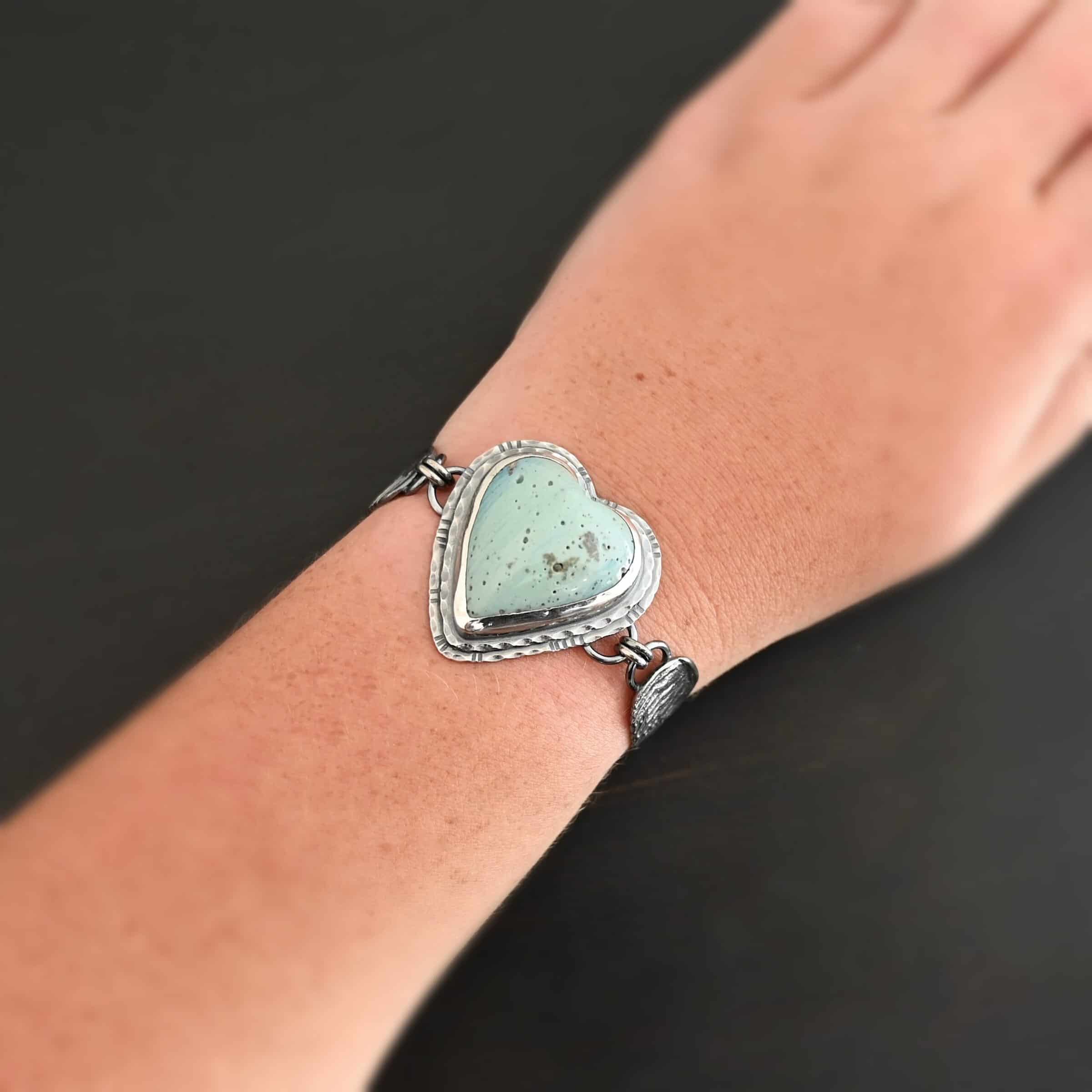 Vanessa Bracelet "Vanessa" Bracelet. The bracelet is a Leland Blue heart with medium sized angel wings on each side. The angel wings curve lightly so they can fit around the wrist. There is two layers of hammered sterling silver around the heart. Bracelet has a silver lobster claw clasp. Bracelet is shown up close by a model.