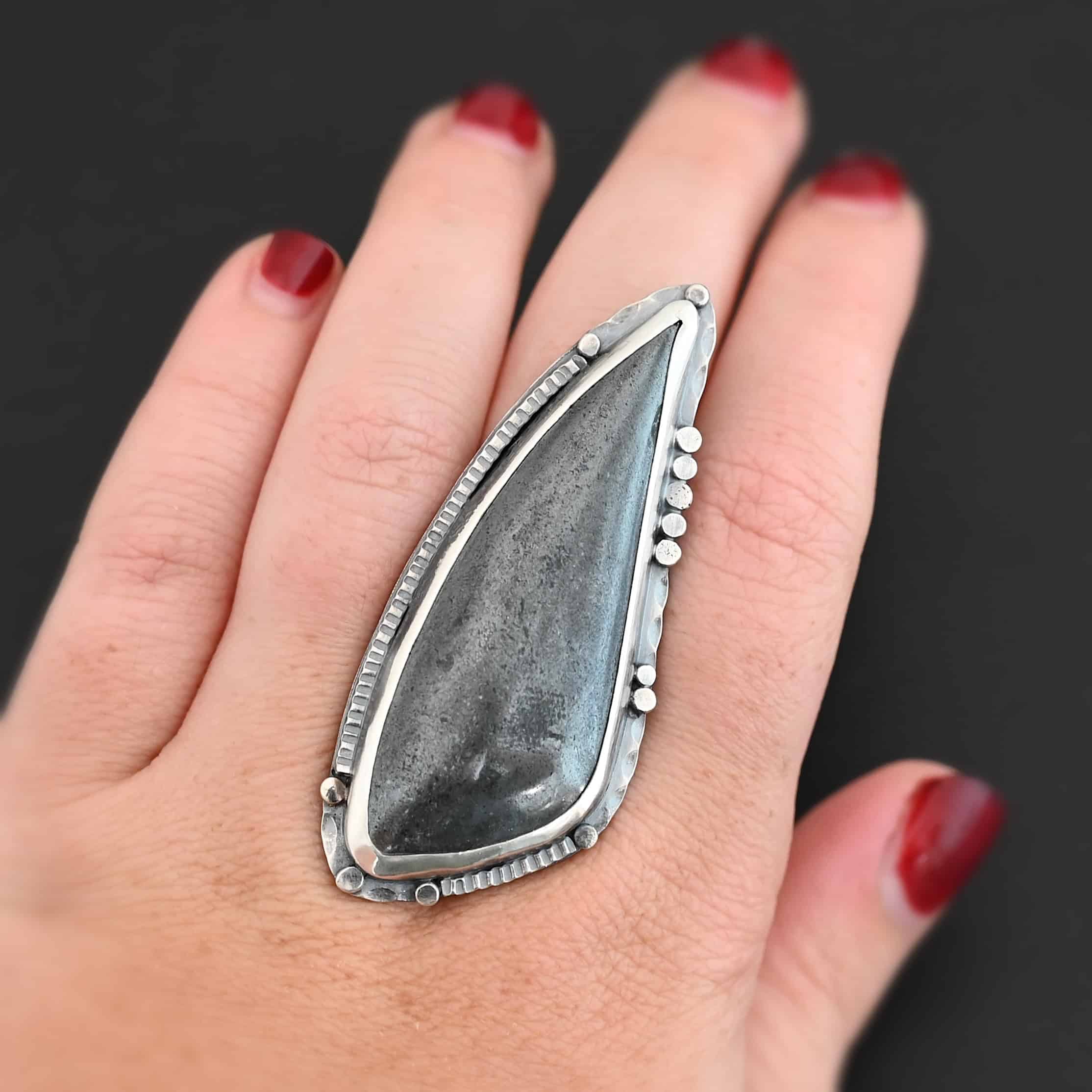 Wandering Star Ring "Wandering Star" Ring. The stone is large, and primarily marquise shaped with a sparkly gray color. The silver around it has hammered lines and flat dots of silver scattered around it. Ring is shown up close by a model.