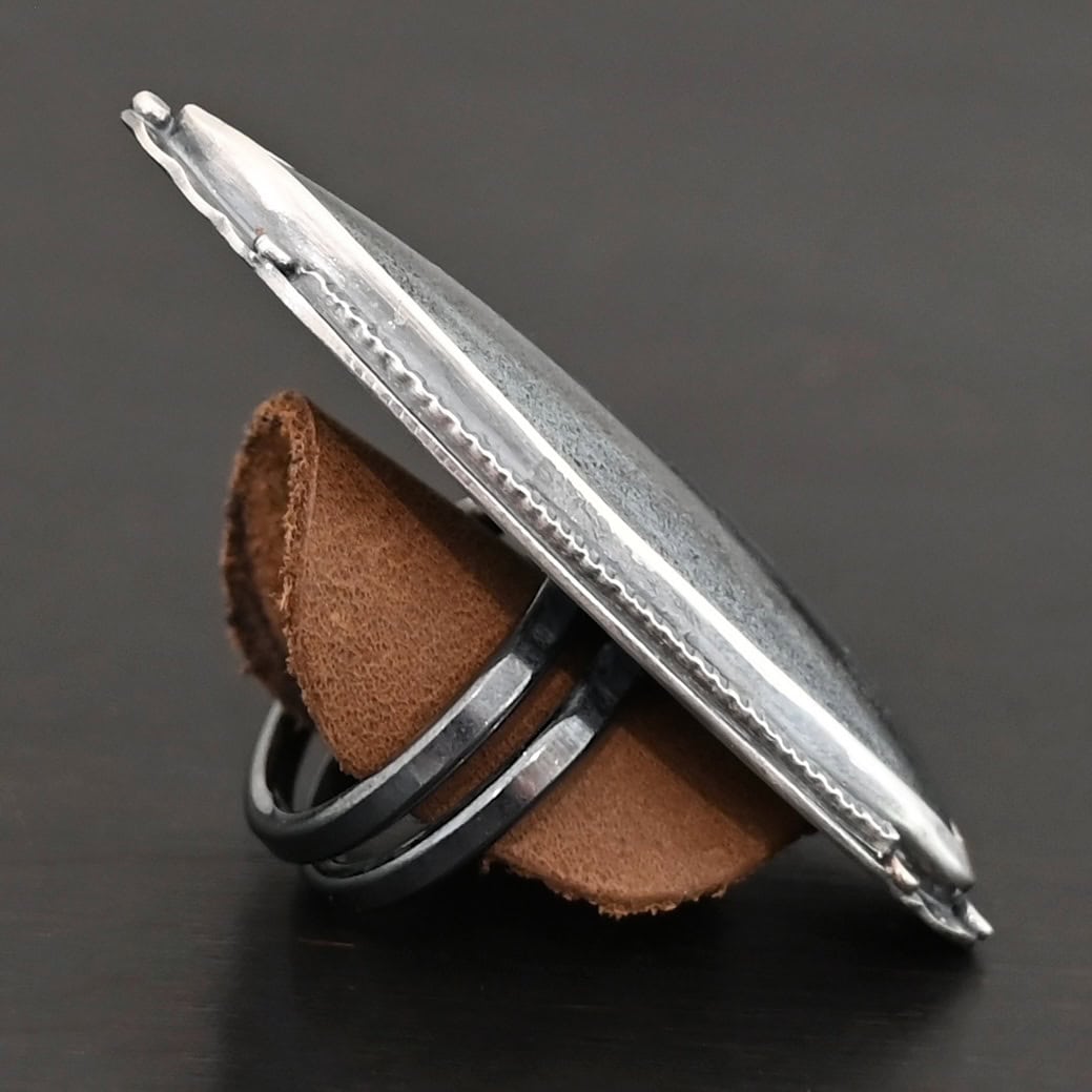 Wandering Star Ring "Wandering Star" Ring. The stone is large, and primarily marquise shaped with a sparkly gray color. The silver around it has hammered lines and flat dots of silver scattered around it. Ring is double banded so it can be adjusted. Ring is sitting on a leather circle so it can stand up straight.