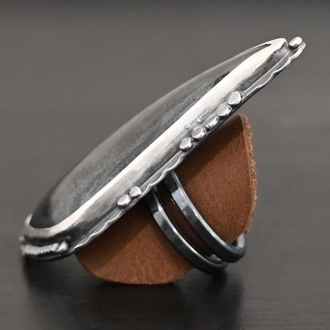 Wandering Star Ring "Wandering Star" Ring. The stone is large, and primarily marquise shaped with a sparkly gray color. The silver around it has hammered lines and flat dots of silver scattered around it. Ring is double banded so it can be adjusted. Ring is sitting on a leather circle so it can stand up straight.
