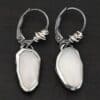 "Gracie" Earrings. The earrings are oval rose cut moonstones hanging vertically. There are silver leverback ear wires with silver wire wrapped around part of them.