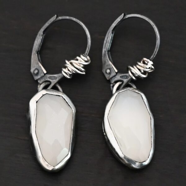 "Gracie" Earrings. The earrings are oval rose cut moonstones hanging vertically. There are silver leverback ear wires with silver wire wrapped around part of them.