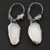 "Gracie" Earrings. The earrings are oval rose cut moonstones hanging vertically. There are silver leverback ear wires with silver wire wrapped around part of them.