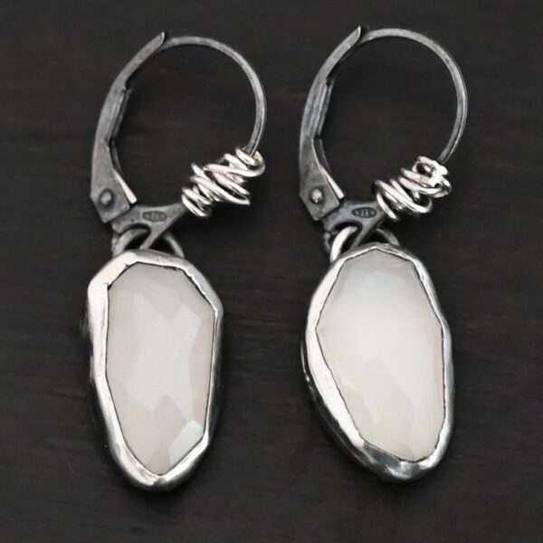 "Gracie" Earrings. The earrings are oval rose cut moonstones hanging vertically. There are silver leverback ear wires with silver wire wrapped around part of them.